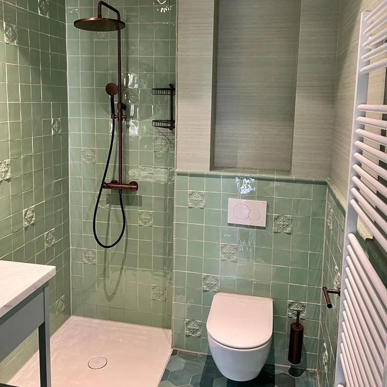 Afgewerkte badkamer met saliegroene reliëftegels, zwarte regendouche en hangend toilet
