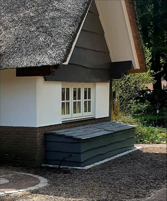Rieten huisje met donkere gevelbekleding in de gevelpunt en de bijpassende kist onder het raam