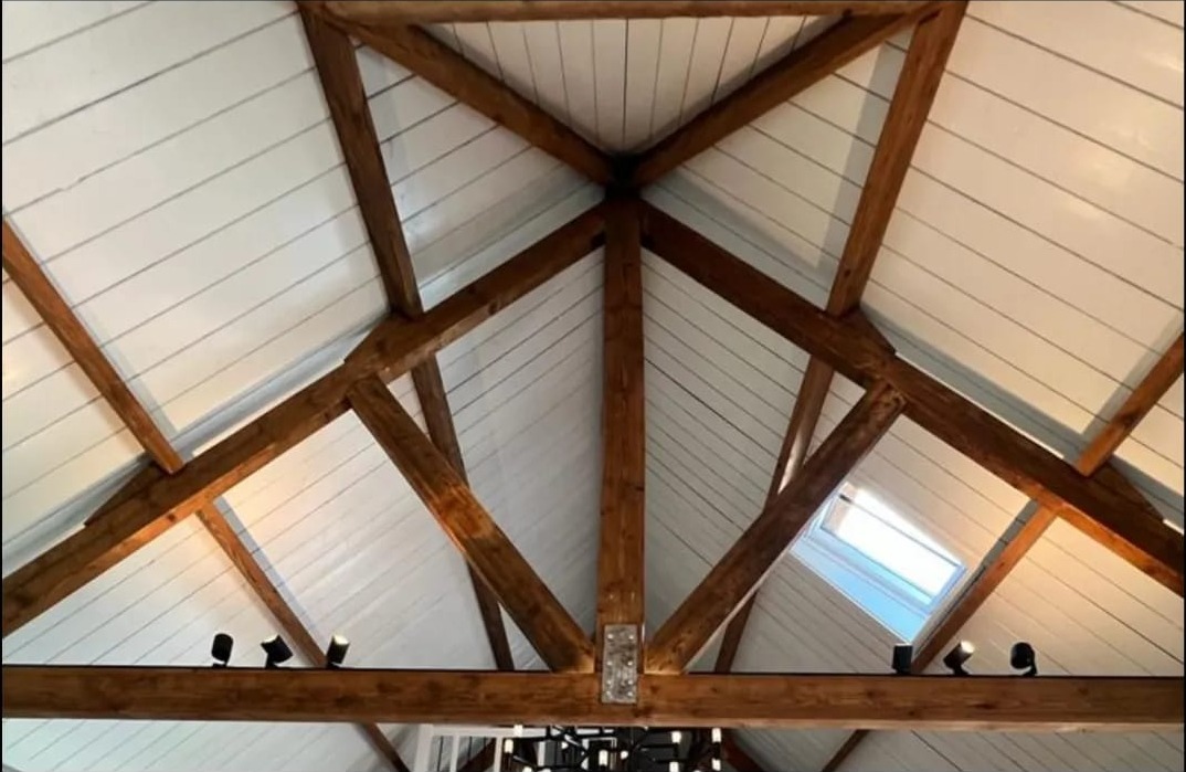 Zichtbare houten spanten onder een wit gepotdekseld plafond met dakramen