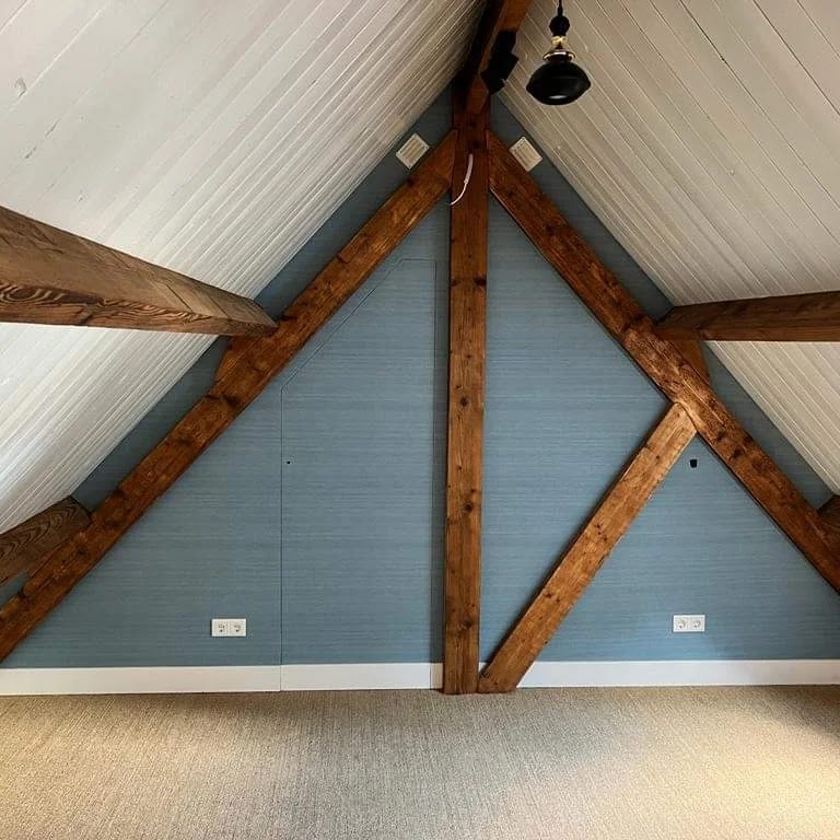 Afgewerkte zolderkamer met donkere houten kapconstructie tegen een blauwe wand